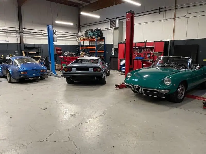 Atelier Retro Mecanic à Lesquin : une Alpine bleue, une Ferrari grise et une Alfa Romeo Spider verte en cours d'intervention