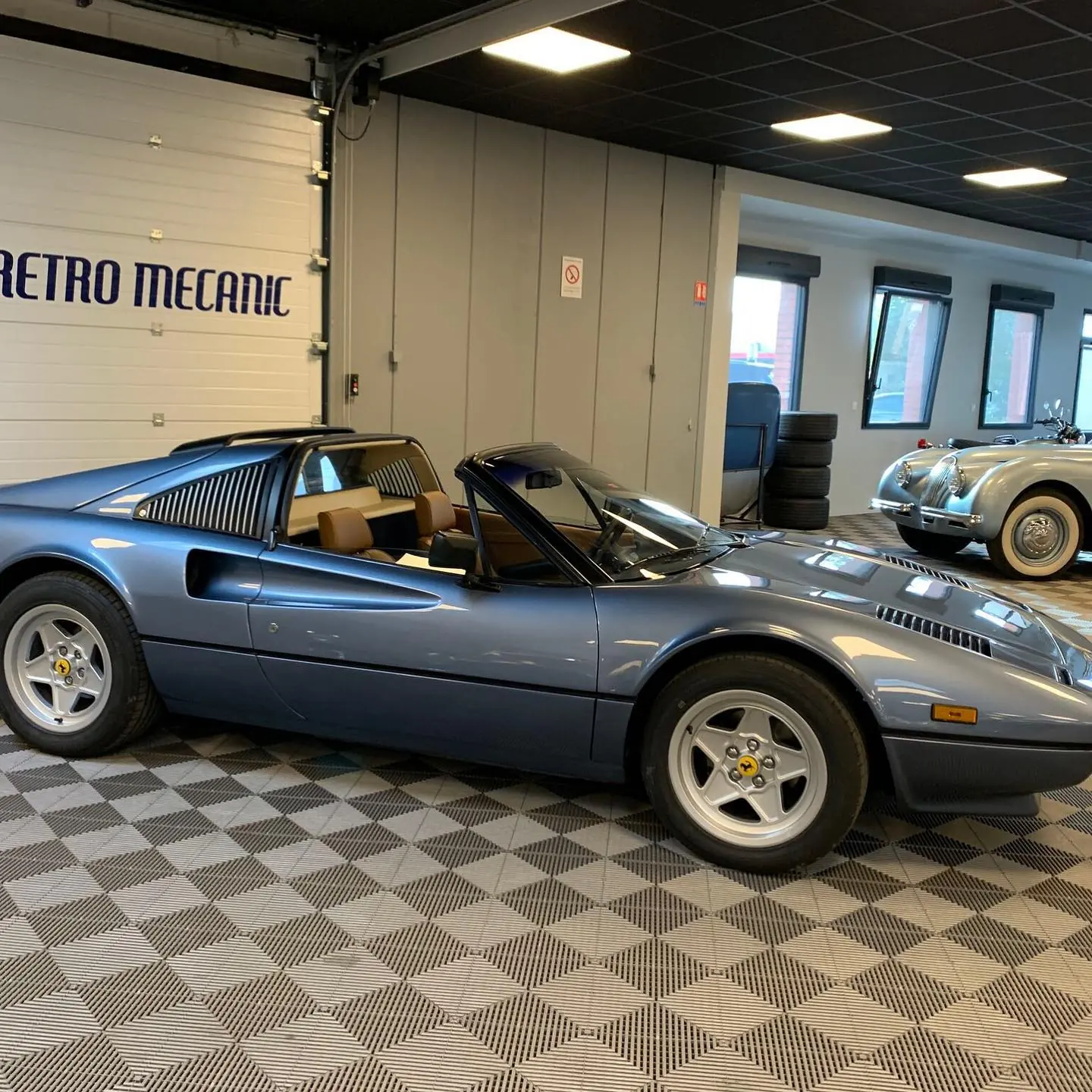 Ferrari 308 GTS bleu métallisé à l'atelier Retro Mecanic, Jaguar XK120 en arrière-plan