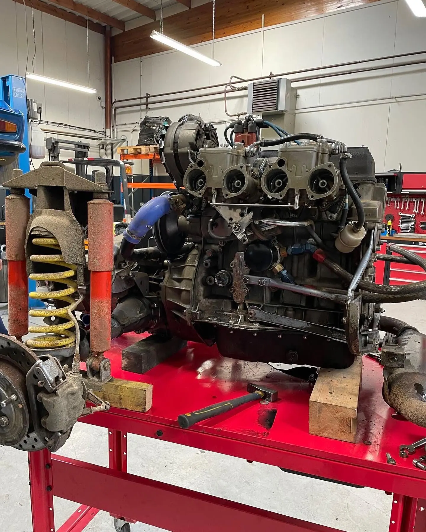Moteur à quatre carburateurs et boîte de vitesses déposés sur un établi à côté d'un train de suspension